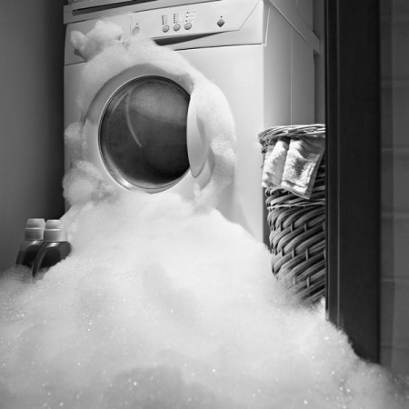 a washing machine with overflowing soap suds in a laundry